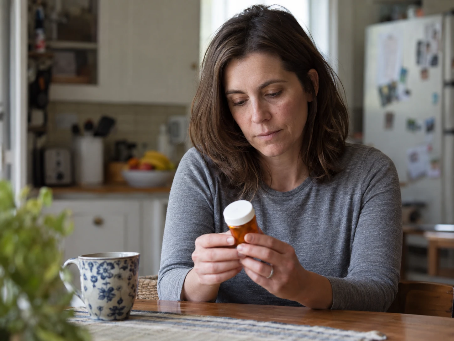 A woman holding a closed amber pharmacy container at a kitchen table
